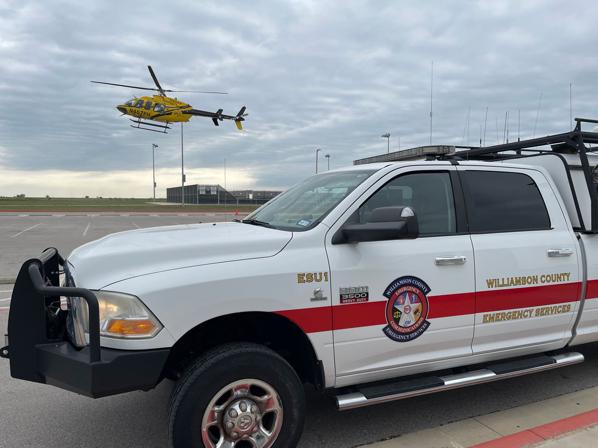 Image of an Emergency Services Truck with a helicopter taking off in the background.